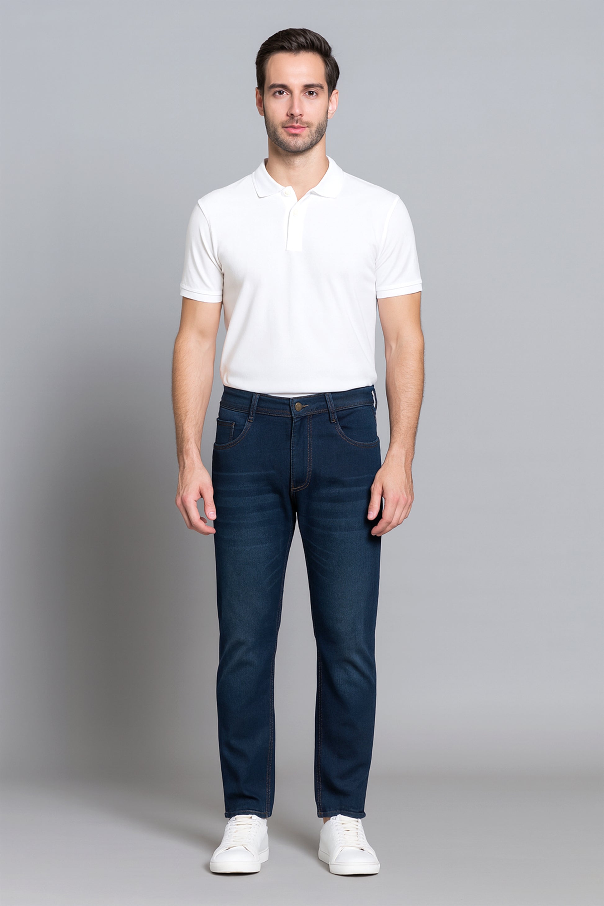 Man wearing a white polo shirt and dark blue jeans on a gray background