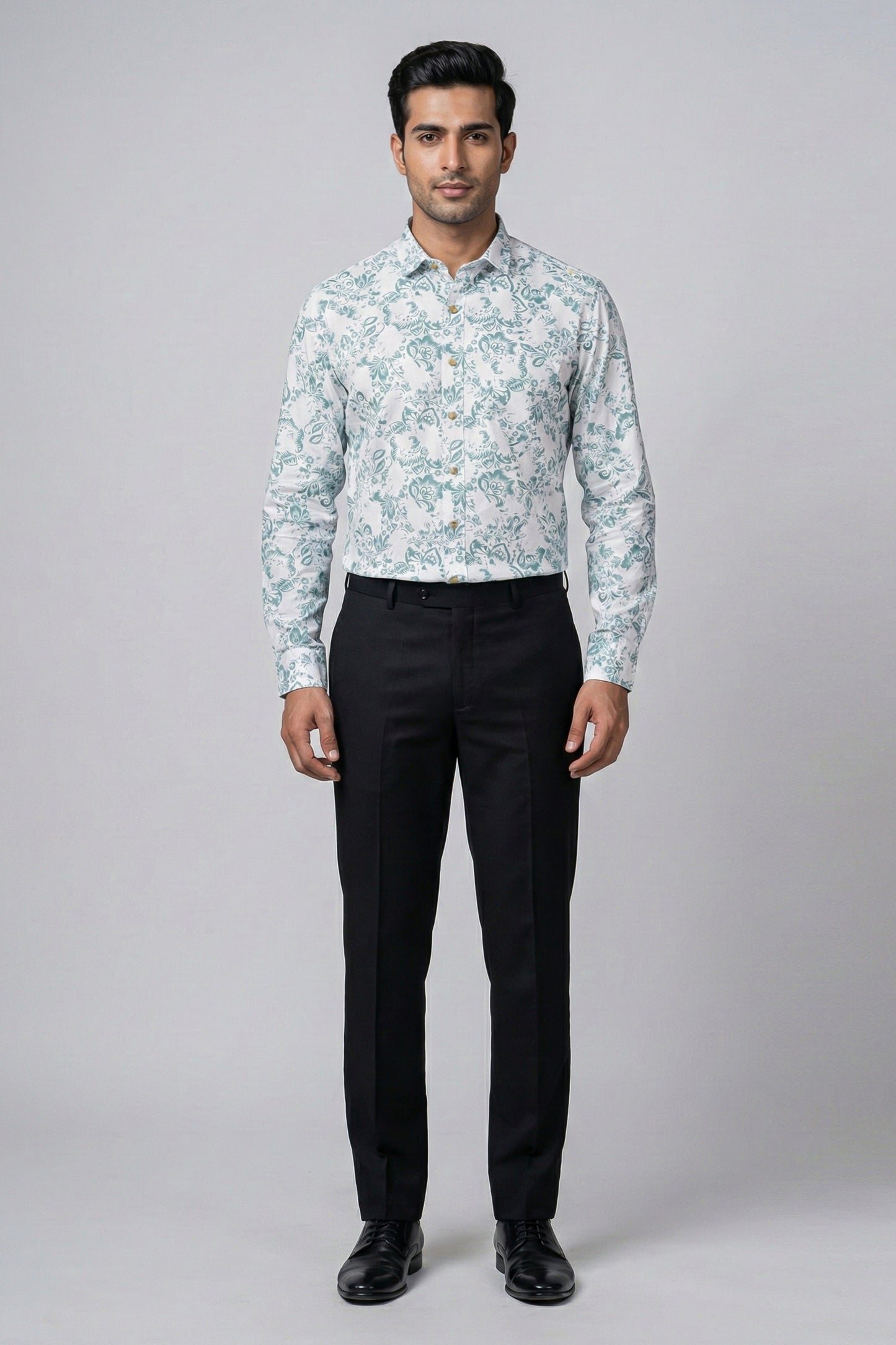 Man wearing a light blue floral shirt and black pants on a gray background