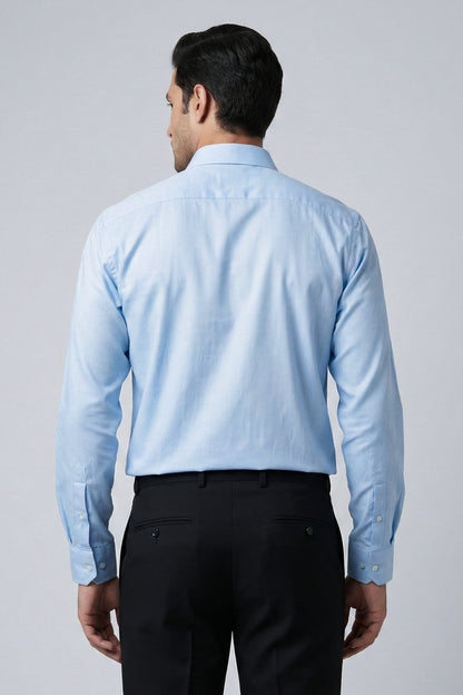 Man wearing a light blue shirt and black pants on a plain background